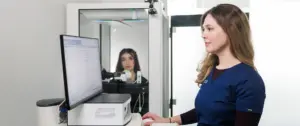 Eine medizinische Praxisassistentin betreut eine Patientin in der Kabine für eine Bodyplethysmographie (grosser Lungenfunktionstest)