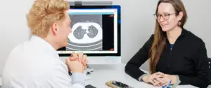 Arzt bespricht die CT-Aufnahme einer Lunge zur Lungenkrebs-Früherkennung im Beratungsgespräch mit einer Patientin