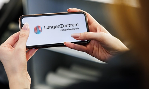 Handy in der Hand mit dem Logo vom LungenZentrum Hirslanden Zürich